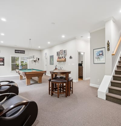 Spacious recreational area featuring a pool table, cozy seating, and an inviting staircase to the upper level.