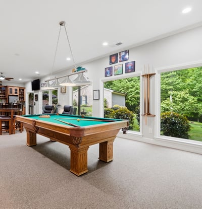 Spacious recreational room featuring a billiard table, large windows, and scenic views of the landscaped yard.