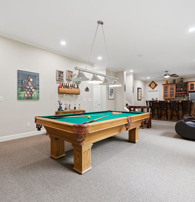 Spacious recreational room featuring a pool table and a well-equipped bar, perfect for entertaining.