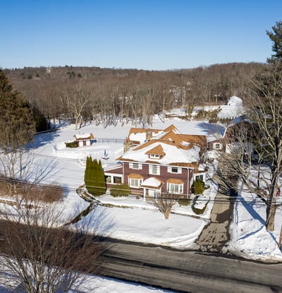 Spacious home nestled in a snowy landscape, featuring ample outdoor space and convenient access to the road.