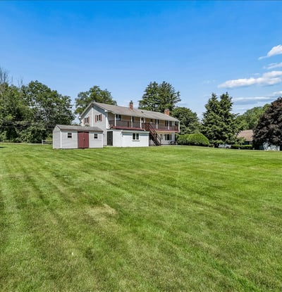 Spacious home on a vast, lush lawn surrounded by mature trees, perfect for outdoor activities and gardening.
