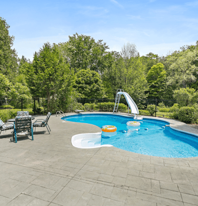 Enjoy summer days by the inviting pool featuring a slide, surrounded by lush greenery and relaxing loungers.