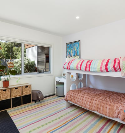 Bright and inviting bedroom featuring bunk beds, ample storage, and a large window overlooking the garden.