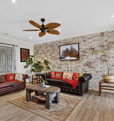 Spacious living area featuring a unique brick wall, rich colors, and a tropical-inspired ceiling fan.