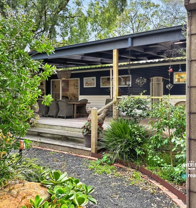 Discover this inviting home with a spacious deck, surrounded by lush landscaping and vibrant greenery.