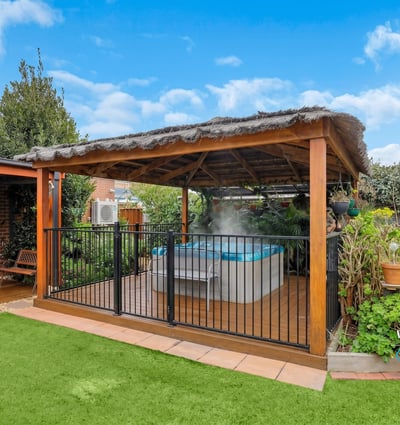 Discover a relaxing outdoor oasis featuring a covered patio and inviting hot tub surrounded by lush greenery.