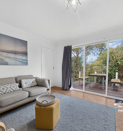 Bright living area featuring large sliding doors that open to a private outdoor deck surrounded by greenery.