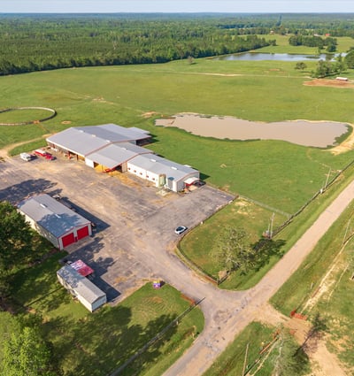 Spacious rural property featuring vast open fields, a pond, and extensive outbuildings for multiple uses.