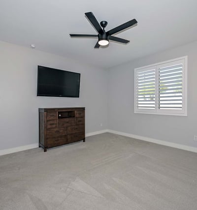 A peaceful primary suite with soft gray tones, upgraded ceiling fan, and bright natural light designed for restful living in this Peoria home.