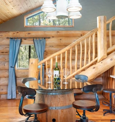 Dining area with handcrafted barrel table, log staircase, and warm wood finishes that reflect the home s authentic Prescott log construction.