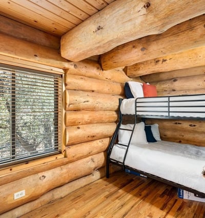Cozy bunk room with log walls and hardwood floors, offering flexible sleeping arrangements while preserving the cabin-style aesthetic.