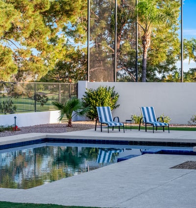 Relax in the backyard retreat featuring a sparkling pool, lounge seating, and serene views framed by mature landscaping.