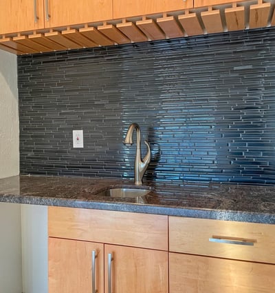Granite counters, warm wood cabinetry, and a glossy backsplash make this wet bar a sophisticated entertaining feature.