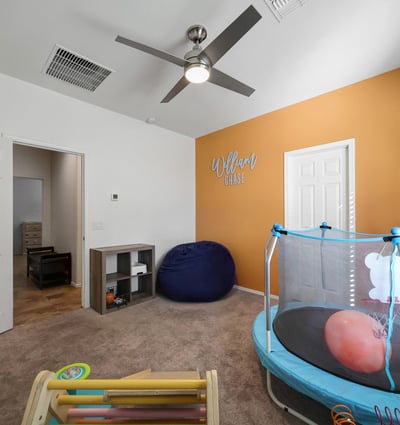 Spacious bedroom with carpet flooring, ceiling fan, and accent wall, offering flexible use for family, guests, or hobbies.