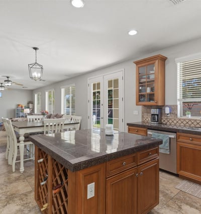 Bright kitchen with wood cabinetry, granite island, tile flooring, and large windows bringing in natural light from the backyard.