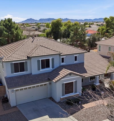 Elevated drone view showing the home's position within the neighborhood with distant mountain scenery and surrounding residential streets in Queen Creek.