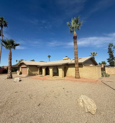 Front yard view showing wide desert landscaping and tall palm trees surrounding this Glendale home. The low-maintenance yard design complements the classic Southwestern architecture.