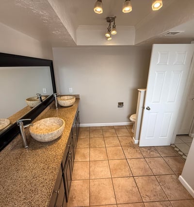 Bathroom featuring dual vessel sinks, long vanity counter, and large mirror. The design provides functionality and style within the primary suite.