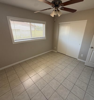 Light-filled bedroom featuring tile flooring, neutral walls, and ceiling fan lighting. The open layout makes the space perfect for guests, family members, or a home office.