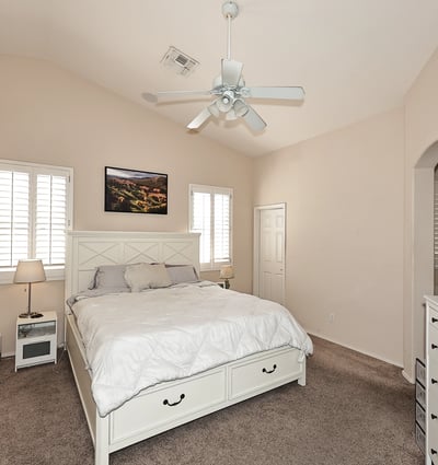 Primary bedroom with vaulted ceilings, ceiling fan, and plantation shutters. This Phoenix home offers a bright and airy space with neutral tones and plush carpet.