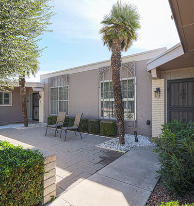 Private courtyard patio with pavers, mature landscaping, and seating area ideal for outdoor entertaining or enjoying quiet mornings in Sun City.