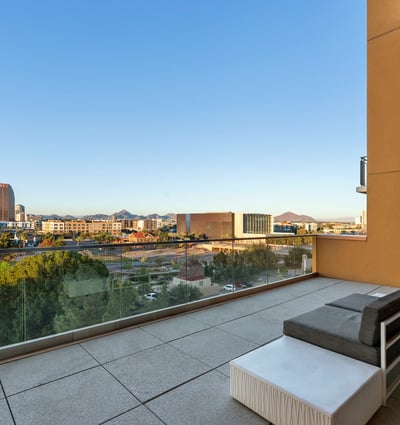 Spacious balcony with modern seating and glass railing, offering beautiful city and park views in Phoenix.
