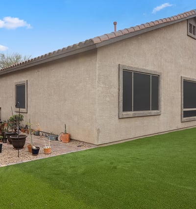 Side yard with patio access and easy-care turf, offering additional usable outdoor space in this Phoenix property.