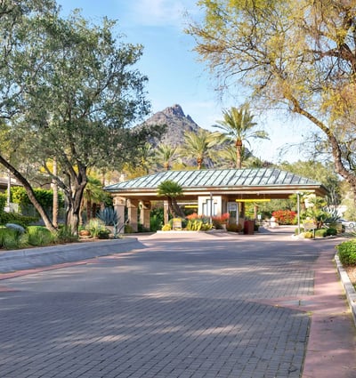 Inviting gated entry with lush landscaping, mature trees, and desert accents, enhancing curb appeal in this Phoenix community.