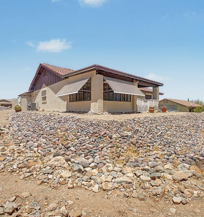 This rear exterior view highlights the home's attractive architecture, mature desert landscaping, and elevated setting. The spacious lot and low-maintenance grounds contribute to the property's appeal in Fountain Hills.