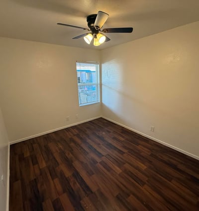 Comfortable bedroom featuring wood-look flooring, ceiling fan, and natural light. The spacious layout provides a relaxing retreat while accommodating a variety of furniture configurations.