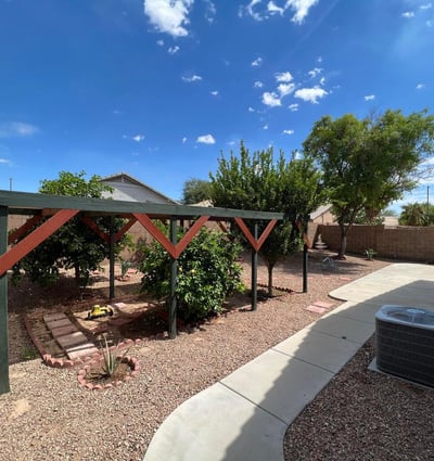 Spacious backyard with mature trees, low-maintenance desert landscaping, and a charming shaded garden structure. An inviting outdoor setting with room to enjoy and personalize.
