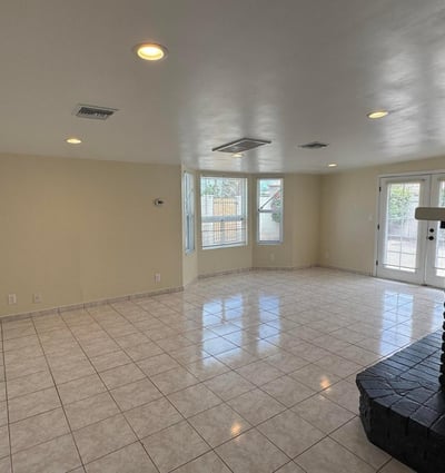 Inviting family room centered around a dramatic fireplace with abundant natural light and backyard access through French doors. The spacious layout offers flexibility for relaxation, entertaining, and indoor-outdoor living.