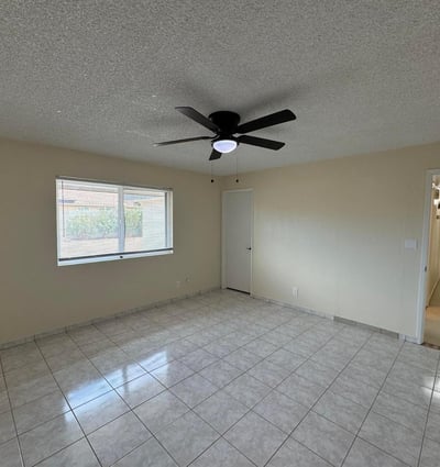 Comfortable guest bedroom featuring neutral finishes, tile flooring, and a ceiling fan. Large windows provide natural light while maintaining a clean, move-in-ready appearance.