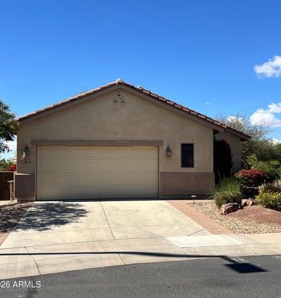 Charming front exterior with mature desert landscaping, spacious driveway, two-car garage, and attractive paver accents creating beautiful curb appeal in a desirable Buckeye neighborhood.