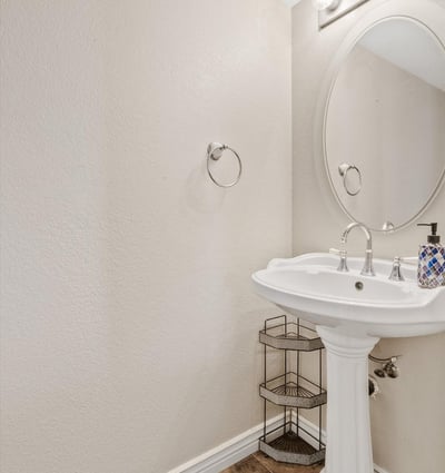 This convenient powder room features a pedestal sink, bright lighting, and neutral finishes, offering both style and functionality for guests and everyday living.
