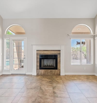 This welcoming family room features a wood-burning fireplace, soaring ceilings, and French doors leading to the covered patio. The spacious layout creates a comfortable gathering place with easy indoor-outdoor flow.