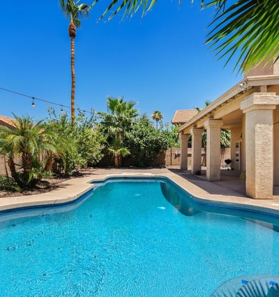 A sparkling swimming pool, mature tropical landscaping, expansive covered patio, and inviting outdoor spaces combine to create a backyard designed for year-round enjoyment in Chandler.