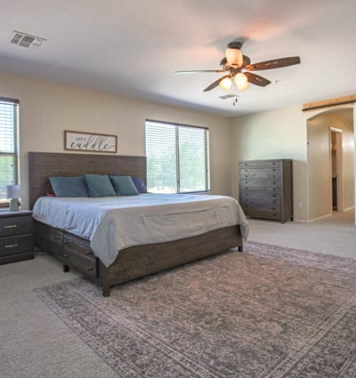 Oversized owner's suite featuring plush carpeting, abundant natural light, ceiling fan, and sliding barn door access to the private en-suite bath. A peaceful retreat in this desirable Waddell home.