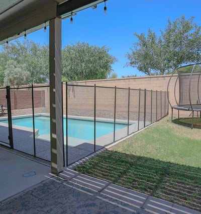 Covered patio overlooking the backyard pool, grassy area, and secure pool fencing, creating a comfortable outdoor retreat for relaxing and entertaining in this Waddell home.