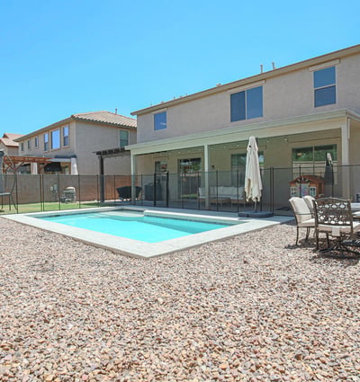 Wide backyard view highlighting the sparkling pool, covered patio, outdoor dining area, and generous outdoor space. A perfect setting for entertaining and enjoying life in Waddell.