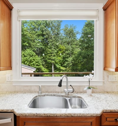 Bright kitchen featuring rich wood cabinetry and a scenic view of lush greenery through a large window.