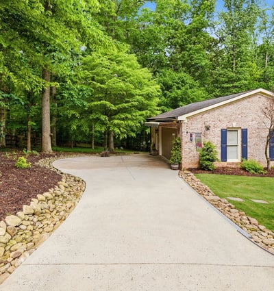 Discover a welcoming home nestled among lush greenery, featuring a spacious driveway and inviting outdoor spaces.