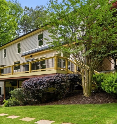 Discover a spacious home with a large deck, surrounded by lush landscaping and vibrant greenery.