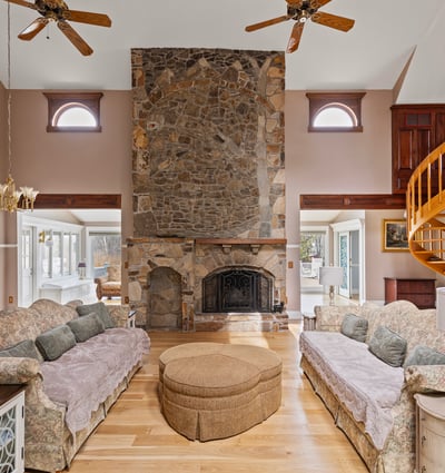 Spacious living area features a striking stone fireplace and unique spiral staircase, perfect for entertaining.