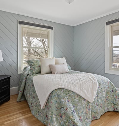 This inviting bedroom features cozy decor, ample natural light, and a tranquil view from the windows.