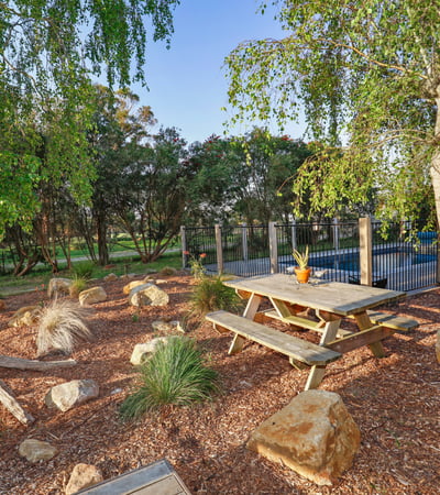 This outdoor space features a picnic area surrounded by native landscaping and a pool in the background.