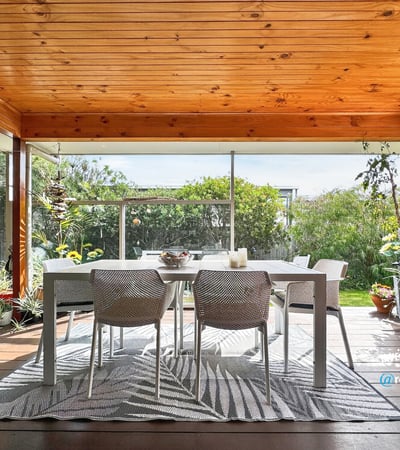 Spacious covered patio surrounded by lush greenery, perfect for outdoor dining and relaxation.