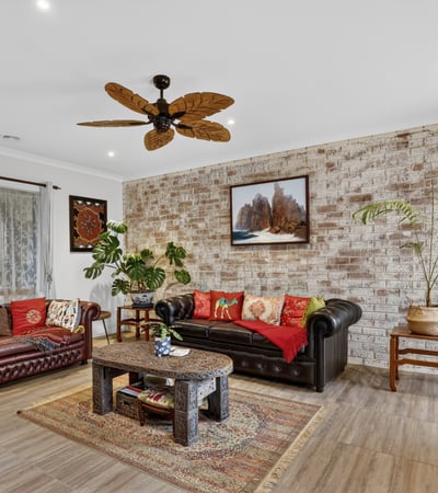 Spacious living area featuring a unique brick wall, rich colors, and a tropical-inspired ceiling fan.