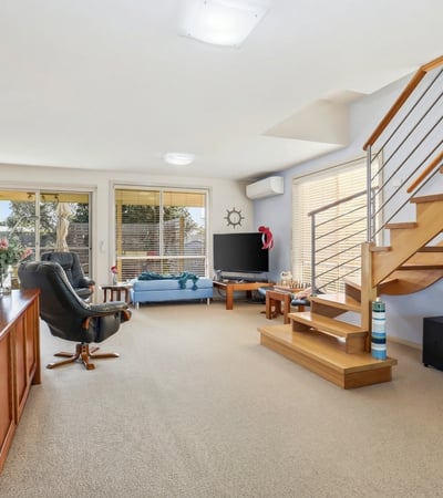 Bright and spacious living area with modern furnishings, featuring a staircase and natural light throughout.