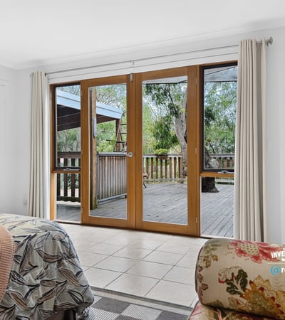 Bright and airy bedroom featuring sliding doors that open to a spacious deck surrounded by greenery.